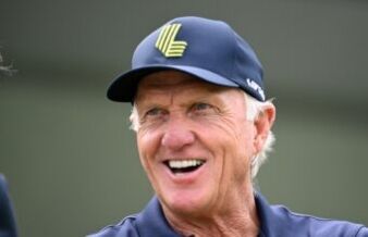Greg Norman Breaks His Silence On LIV Golf’s Future Older man smiling, wearing a blue cap with a neon-green emblem on the front.