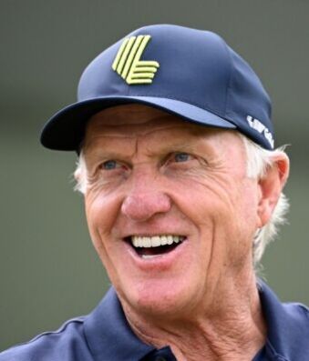 Greg Norman Breaks His Silence On LIV Golf’s Future Older man smiling, wearing a blue cap with a neon-green emblem on the front.