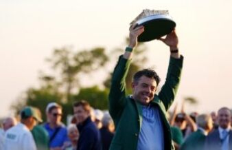 Rory McIlroy’s Decision Has Golf Fans Criticizing PGA Tour Man in a green jacket proudly raises a large circular model boat above his head at an outdoor crowd event, smiling for the camera.