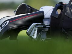 A 10-Handicap and a +4-Handicap Got Fitted—Then This Happened Close-up of a golf bag with a Titleist iron resting beside it on a blurred green background, highlighting black and white bag details with a red stripe.