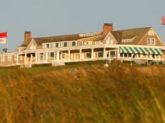 Father’s Day Golf Gifts to Save Dad a Trip to the Pro Shop Coastal golf clubouse on a hill, with white porch, green-and-white striped awning, flags, and people on the grass in the foreground.