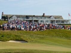 Shinnecock Hosts U.S. Open Amidst Preparations to Avoid Past Issues Large crowd of spectators gathered on a grassy hill outside a white clubhouse watching a golf event, with an American flag on the right.