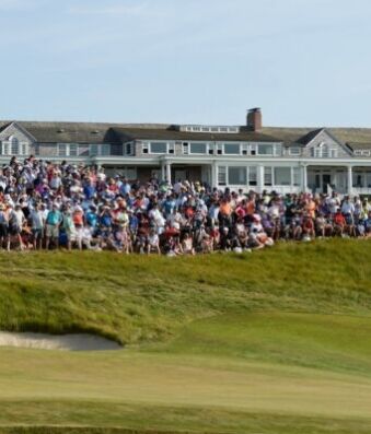 Shinnecock Hosts U.S. Open Amidst Preparations to Avoid Past Issues Large crowd of spectators gathered on a grassy hill outside a white clubhouse watching a golf event, with an American flag on the right.