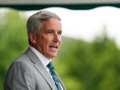 Jay Monahan Unloads on Team USA’s Curtis Cup Challenges Older man in a light gray suit, seen in profile, speaking outdoors with a blurred green background.