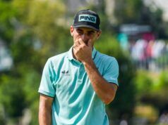 Joaquin Niemann Receives Two-Stroke Penalty for ‘Serious Misconduct’ at US Open Male golfer in a turquoise polo shirt and black Ping cap touches his face while standing outdoors on a sunny golf course behind him blurred trees and spectators
