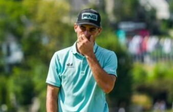 Joaquin Niemann Receives Two-Stroke Penalty for ‘Serious Misconduct’ at US Open Male golfer in a turquoise polo shirt and black Ping cap touches his face while standing outdoors on a sunny golf course behind him blurred trees and spectators