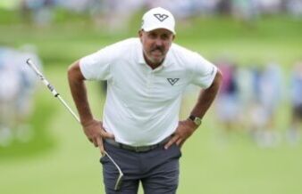 Phil Mickelson’s Latest Controversy Will Test Golf’s Patience Male golfer in a white polo and cap stands with hands on hips on a lush green course, holding a club.