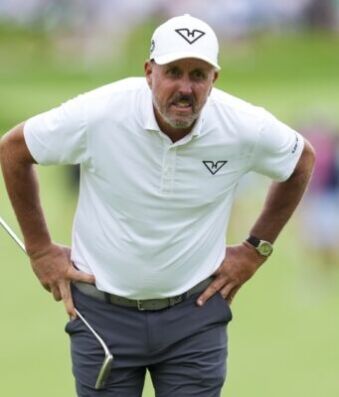 Phil Mickelson’s Latest Controversy Will Test Golf’s Patience Male golfer in a white polo and cap stands with hands on hips on a lush green course, holding a club.