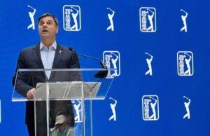 PGA Tour Unveils Two-Track System for 2028 Man in a dark suit giving a speech at a clear podium with a microphone against a blue PGA TOUR backdrop.