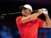 Tiger Woods Introduces Major PGA Tour Reforms in Rare Appearance Male golfer in a red polo shirt and white cap mid-swing, gripping a golf club against a dark background.