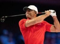 Tiger Woods Introduces Major PGA Tour Reforms in Rare Appearance Male golfer in a red polo shirt and white cap mid-swing, gripping a golf club against a dark background.