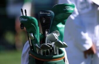 GolfWRX Reveals Why Dads Should Unload Golf Gear for Power Tools Close-up of a golf bag with multiple clubs, showing Titleist and TaylorMade branding outside on a sunny day.