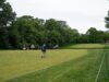 Indiana Rookie Emerges as LPGA’s Sole Left-Handed Player Golf course with several players walking and carrying golf bags near lush trees, a green fairway in the distance.