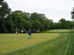 Indiana Rookie Emerges as LPGA’s Sole Left-Handed Player Golf course with several players walking and carrying golf bags near lush trees, a green fairway in the distance.