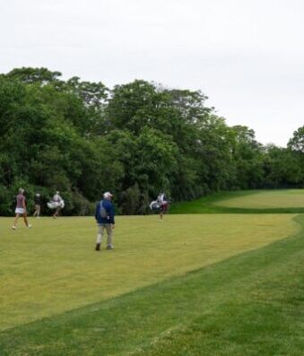 Indiana Rookie Emerges as LPGA’s Sole Left-Handed Player Golf course with several players walking and carrying golf bags near lush trees, a green fairway in the distance.