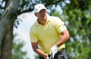 Koepka Fires Eight Birdies, Takes Early Canadian Open Lead Golfer in a pale yellow polo and white cap mid-swing on a sunny golf course