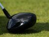 Just Announced: Tour Edge Exotics Reveals New Mini Driver Tech Close-up of a glossy black golf driver head on green grass with a light gray shaft visible nearby.