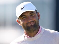 Scottie Scheffler Downplays Grand Slam Motivation at US Open Close-up of a man wearing a white Nike cap, smiling outdoors with a blurred background.