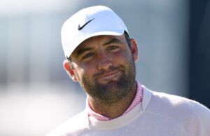 Scottie Scheffler Downplays Grand Slam Motivation at US Open Close-up of a man wearing a white Nike cap, smiling outdoors with a blurred background.