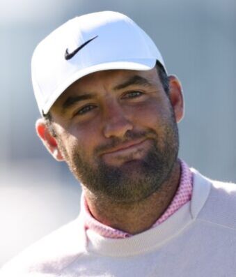 Scottie Scheffler Downplays Grand Slam Motivation at US Open Close-up of a man wearing a white Nike cap, smiling outdoors with a blurred background.