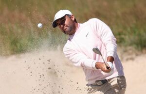 Scheffler Favored to Win 2026 U.S. Open, But Longest Odds Since 2023 Golfer in a light pink sweater and white cap hitting from a bunker as sand sprays into the air near a golf ball and club