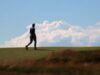 Shinnecock Hills Qualifiers Secure Spots at The Masters and US Open Blurry silhouette of a person walking on a grassy hill against a blue sky with fluffy clouds.