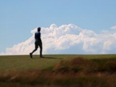 Shinnecock Hills Qualifiers Secure Spots at The Masters and US Open Blurry silhouette of a person walking on a grassy hill against a blue sky with fluffy clouds.
