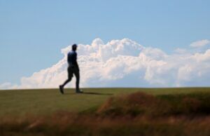Shinnecock Hills Qualifiers Secure Spots at The Masters and US Open Blurry silhouette of a person walking on a grassy hill against a blue sky with fluffy clouds.