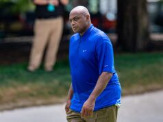 Barkley Remains Longest Shot to Win Celeb Tourney Man wearing a bright blue Nike polo shirt walking outdoors along a park path.