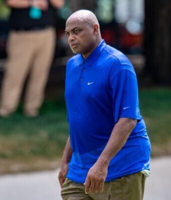 Barkley Remains Longest Shot to Win Celeb Tourney Man wearing a bright blue Nike polo shirt walking outdoors along a park path.