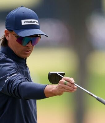 Fowler’s Putter Experiments Continue at John Deere Classic Golfer wearing a navy Cobra cap and mirrored sunglasses, gripping a golf club mid-swing.