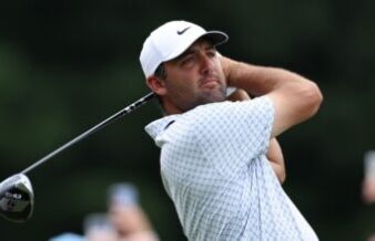 Scottie Scheffler Targets Historic Double Win in Scotland Male golfer in a white cap swinging a golf club, focused on the ball, on a green course backdrop.