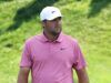 Scheffler Stuns Field as Scottish Open Showdown Begins Man wearing a pink polo shirt and white Nike cap standing in a grassy outdoor area with greenery in the background.