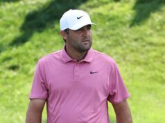 Scheffler Stuns Field as Scottish Open Showdown Begins Man wearing a pink polo shirt and white Nike cap standing in a grassy outdoor area with greenery in the background.