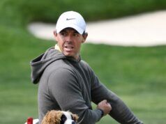 Rory McIlroy Reveals How He Got Devil Wears Prada 2 Role Man in a gray hoodie and white Nike cap looks to the side outdoors with a small plush dog visible in the foreground.