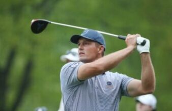 Bryson DeChambeau Lays Out 2 Demands for PGA Tour Return Golfer in a blue cap and striped shirt mid-swing on a golf course, glove on his left hand.