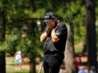 Humiliating Moment Golfer Hits ‘One Of The Worst Shots EVER’ Male golfer in a black cap and polo covering his face with both hands outdoors, holding a golf club at his side.
